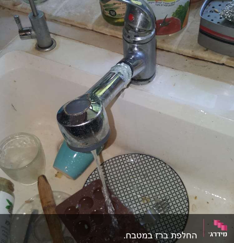 ברז מטבח עם מים זורמים בכיור מלא כלים